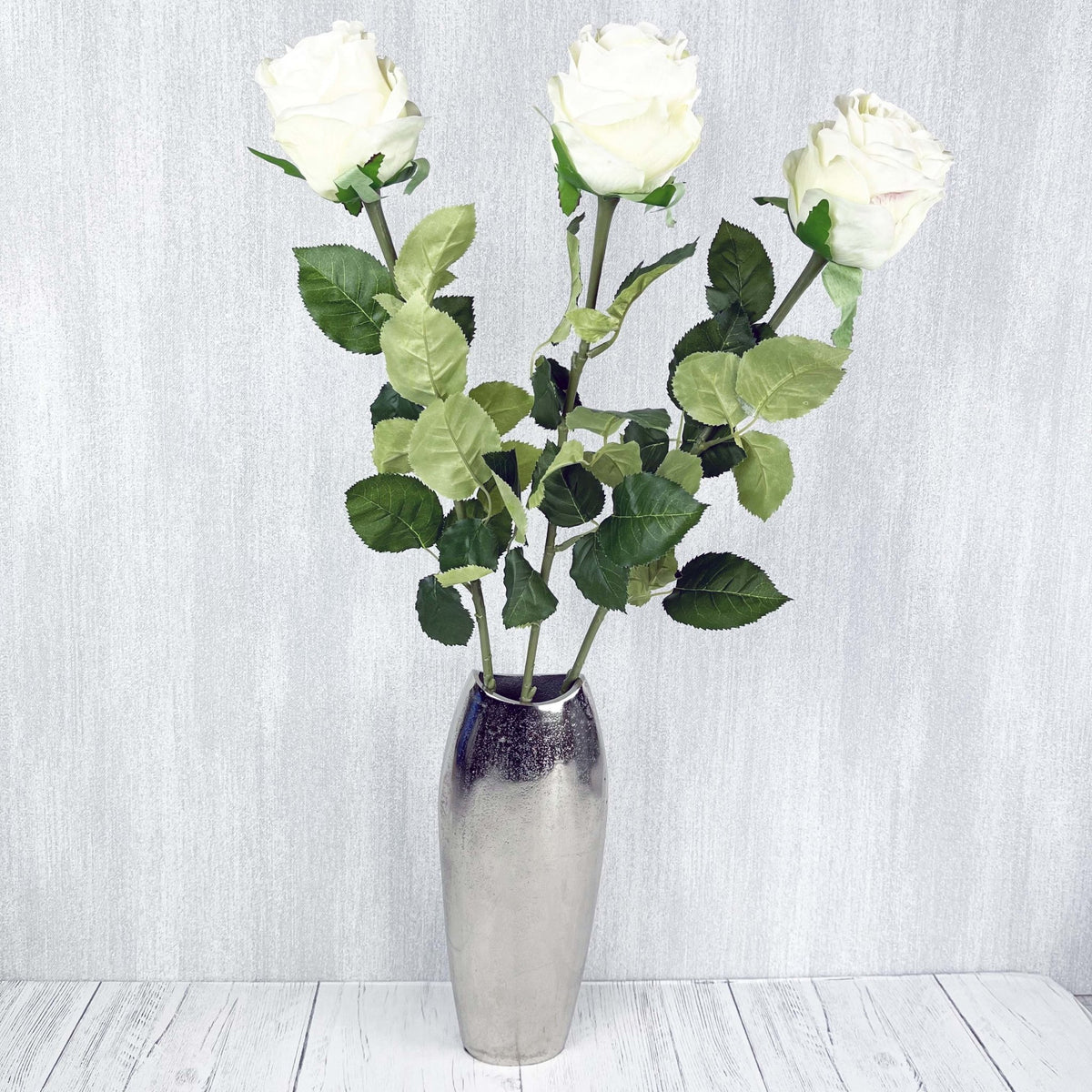 Traditional White Roses in chrome vase on grey background.