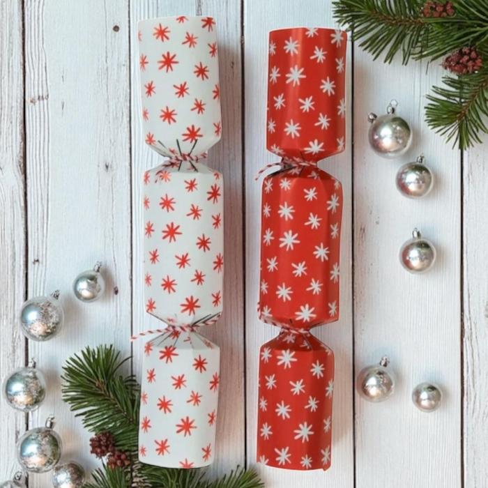 Two Christmas crackers with star patterns on a white background with silver baubles and greenery. 