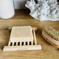 Bath products including a scrubber, brush, and soap holder on a wooden surface with coral decor.