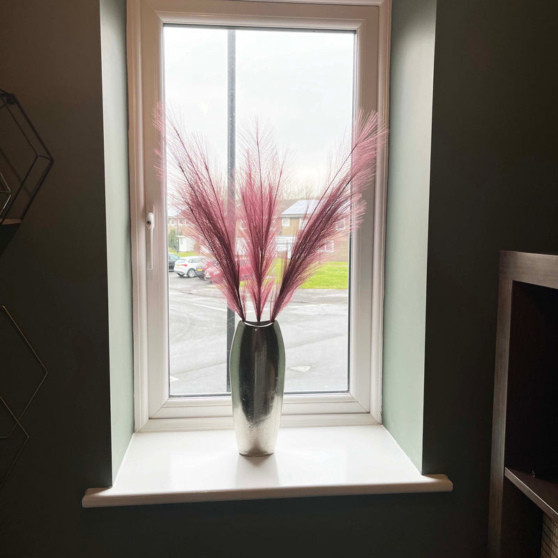 Scarlet Red Faux Pampas Grass Stem in a chrome vase on a window sill.