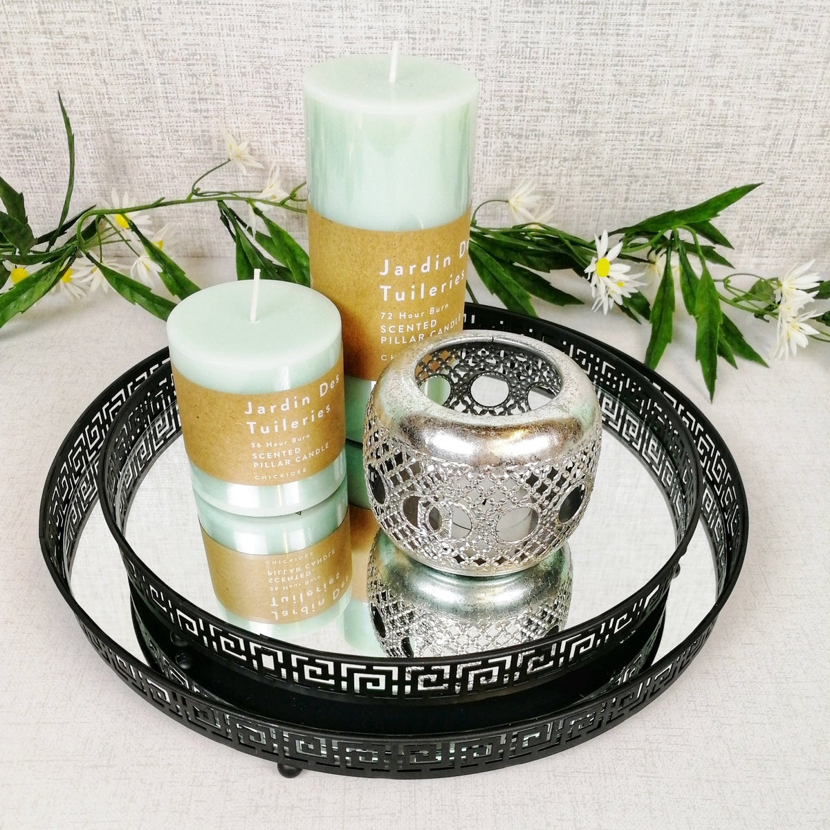 Black decorative circle mirror trays stacked with green scented pillar candles and a silver tea light holder