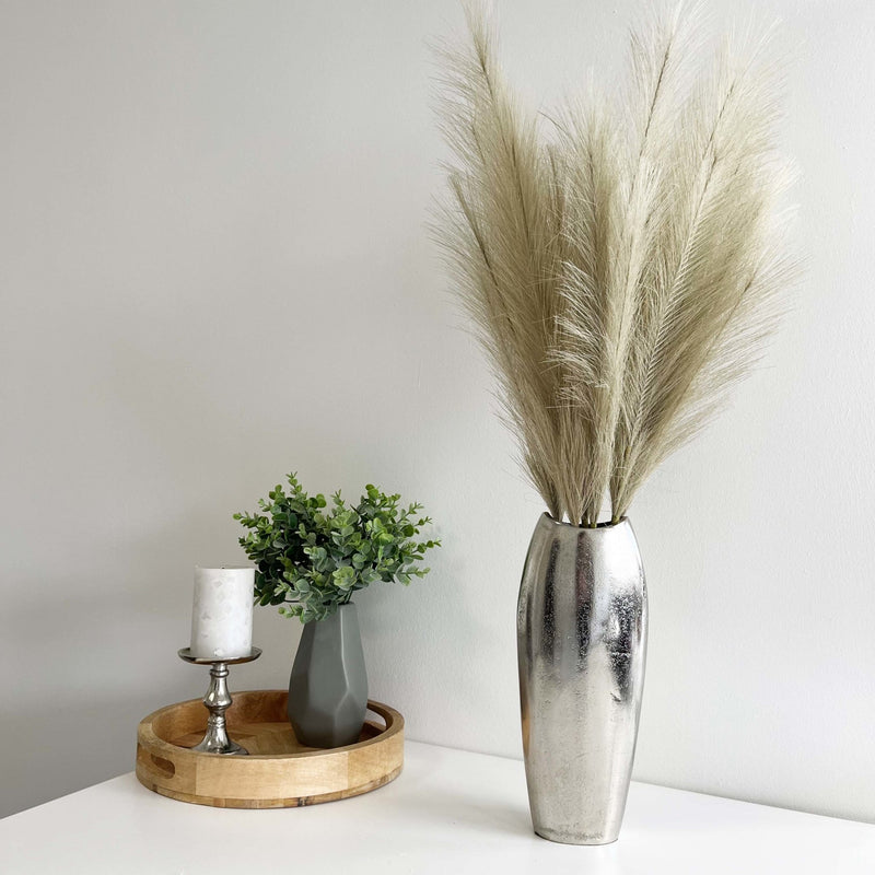 Bleached Faux Pampas Grass Stems in chrome vase with wooden tray and green plant and candle.