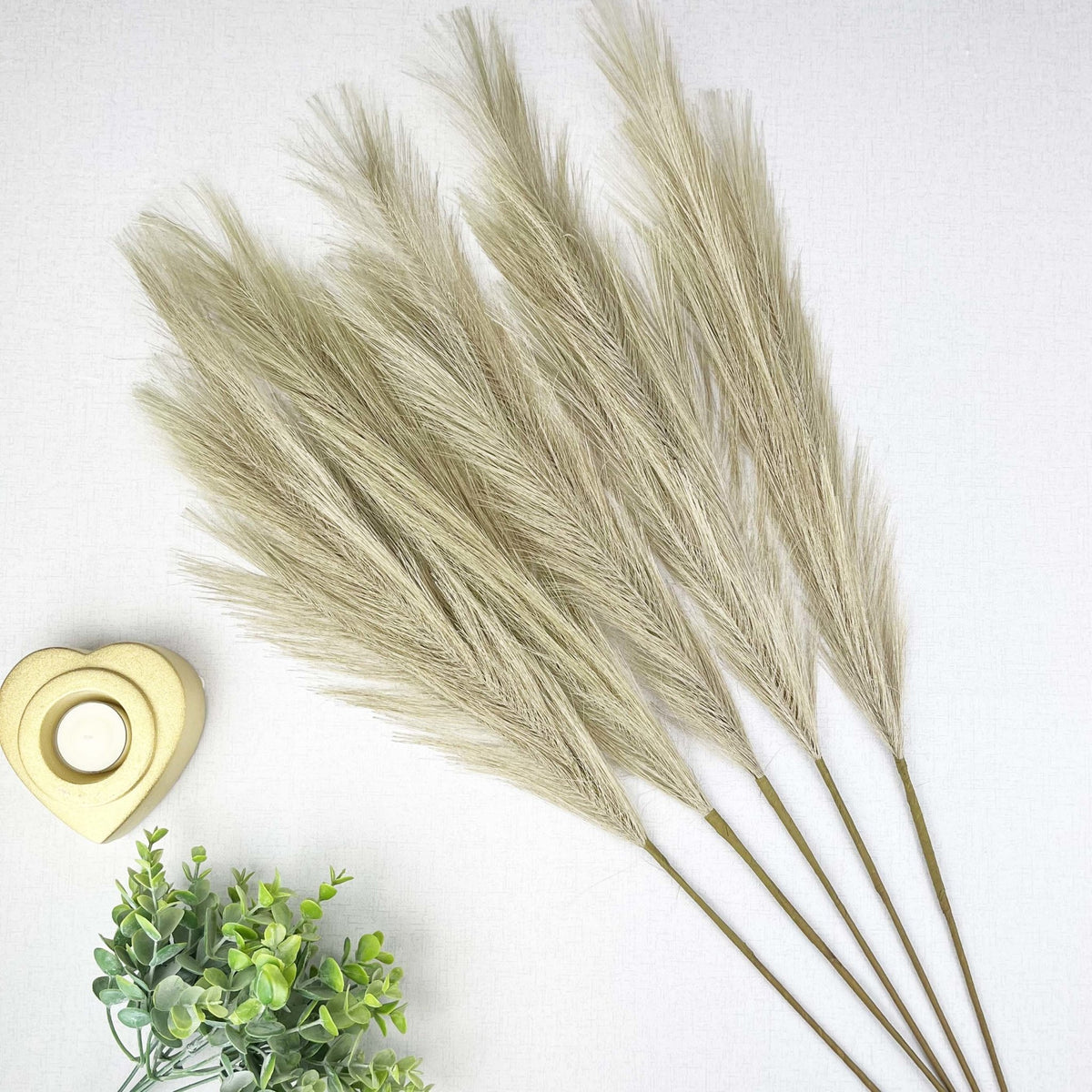 Bleached Faux Pampas Grass Stems on white background with gold heart tealight holder and greenery.