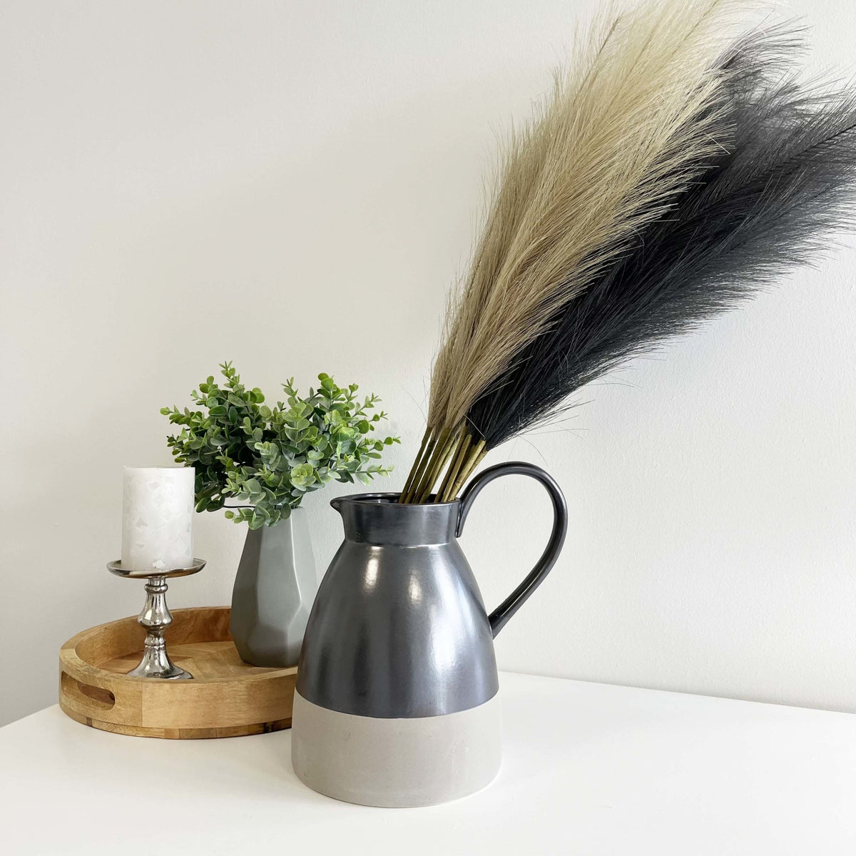 Bleached Faux Pampas Grass Stems in grey vase with wooden tray and green plant and candle.