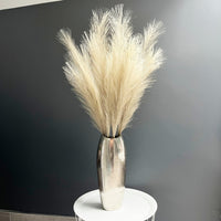 Bleached Faux Pampas Grass Stem in chrome vase, one white table, with dark grey background.