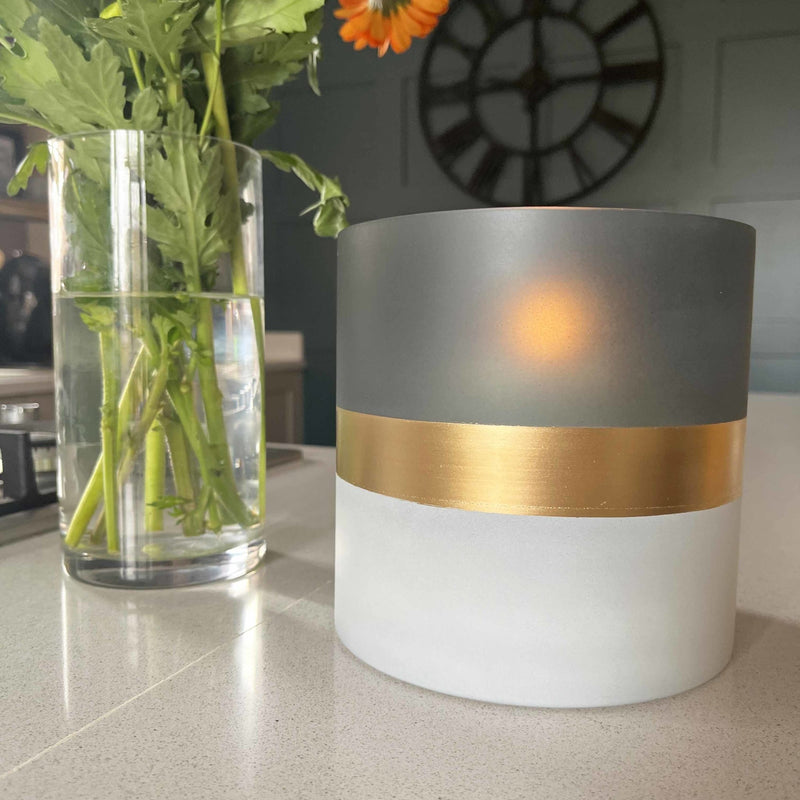 Contra Frosted Glass Votive Candle Holder with lit candle, on kitchen bench with flowers and clock in background