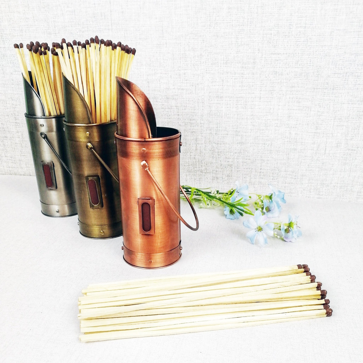 Matchstick holders bronze pewter copper with matches and flowers blue against grey background