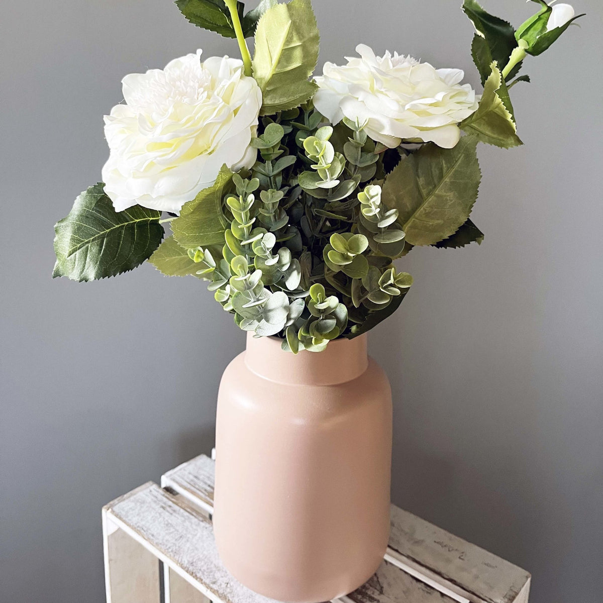 Full leaf sprays with white garden roses in a pink vase.