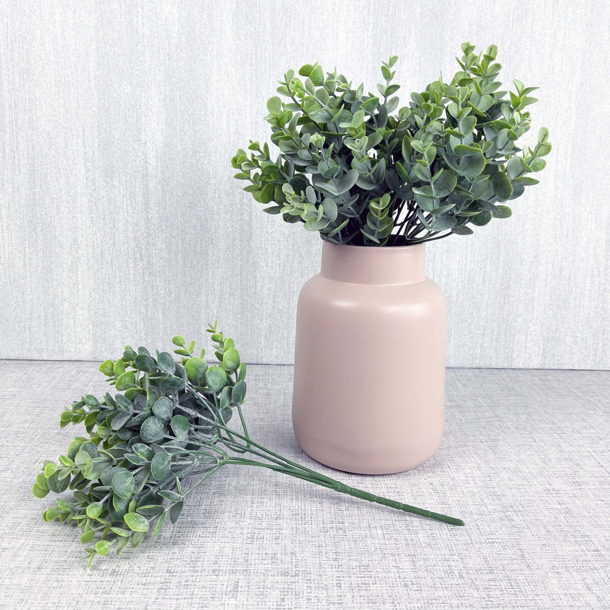 Full leaf sprays in pink vase on grey background.