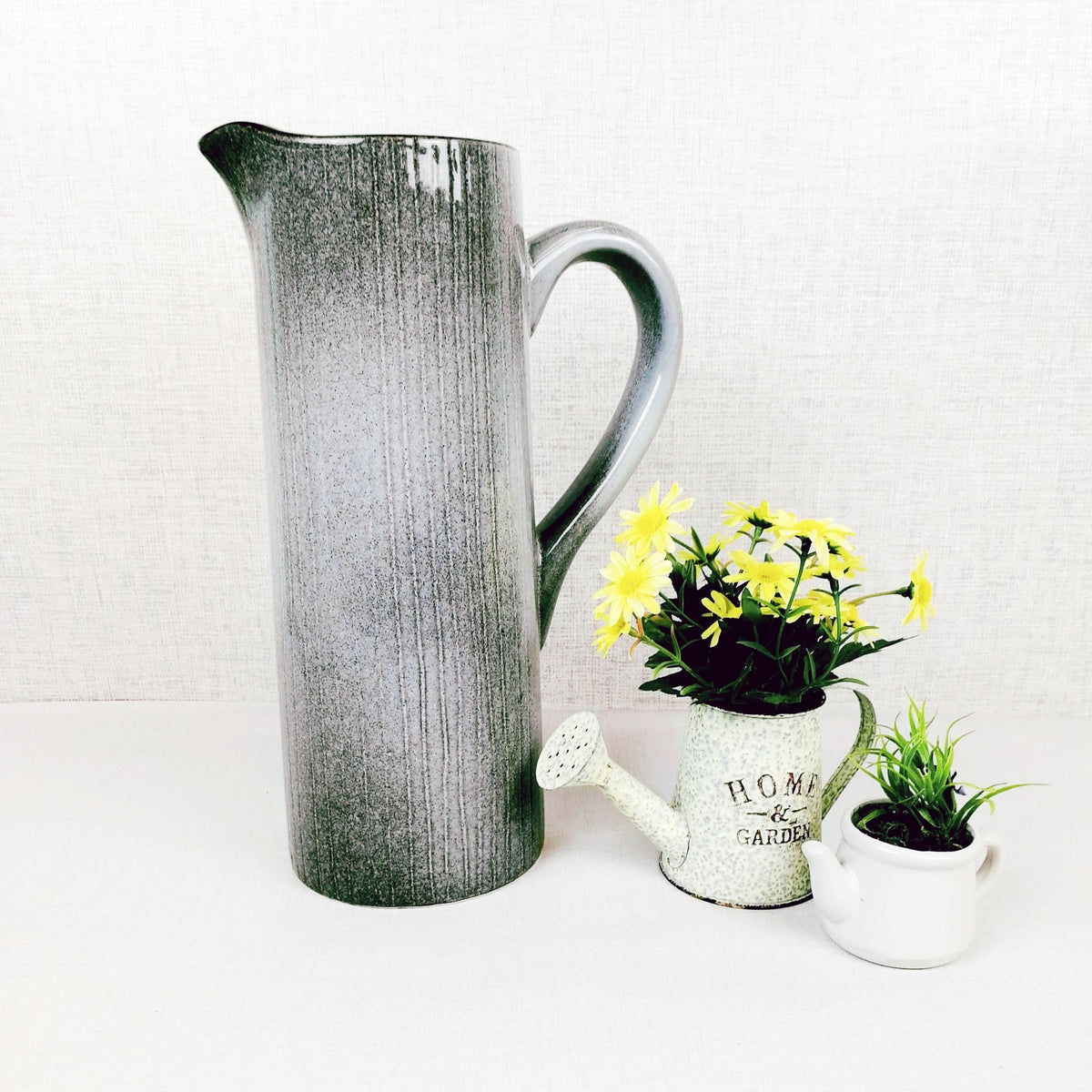 Gradus Ceramic Grey Jug next to a watering can planter with yellow flowers and a white planter