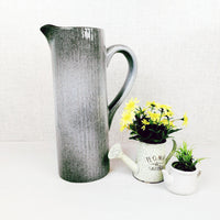 Gradus Ceramic Grey Jug next to a watering can planter with yellow flowers and a white planter