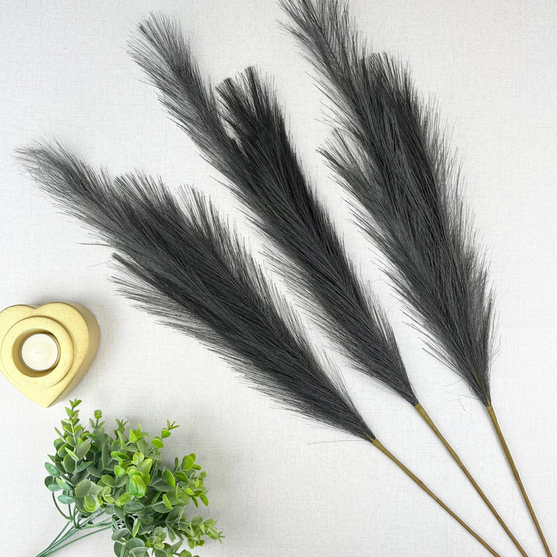Grey Faux Pampas Grass Stem on white background, with a gold heart tealight holder and greenery.