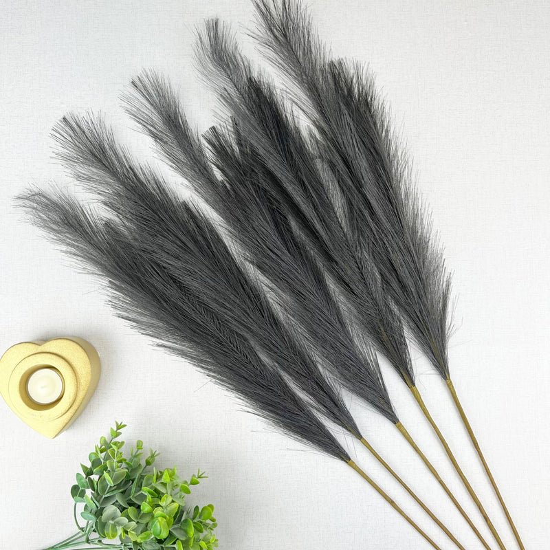 Grey Faux Pampas Grass Stem on white background, with a gold heart tealight holder and greenery.