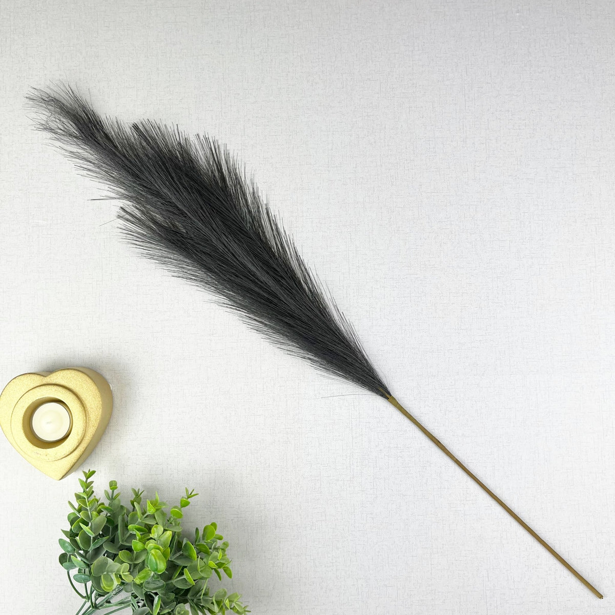 Grey Faux Pampas Grass Stem on white background, with a gold heart tealight holder and greenery.
