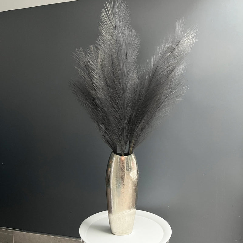 Grey Faux Pampas Grass Stem in a chrome vase on white table, with a dark grey background.