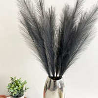 Grey Faux Pampas Grass Stems in a chrome vase with a candle and plant on a copper tray.