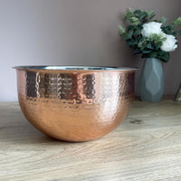 Large Hammered Copper-style Bowl on dining table with flower vase in background
