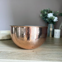 Large Hammered Copper-style Bowl on a kitchen table with vase and candle in background