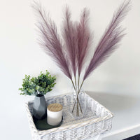 Lilac Faux Pampas Grass Stem in glass vase with plant and candles.