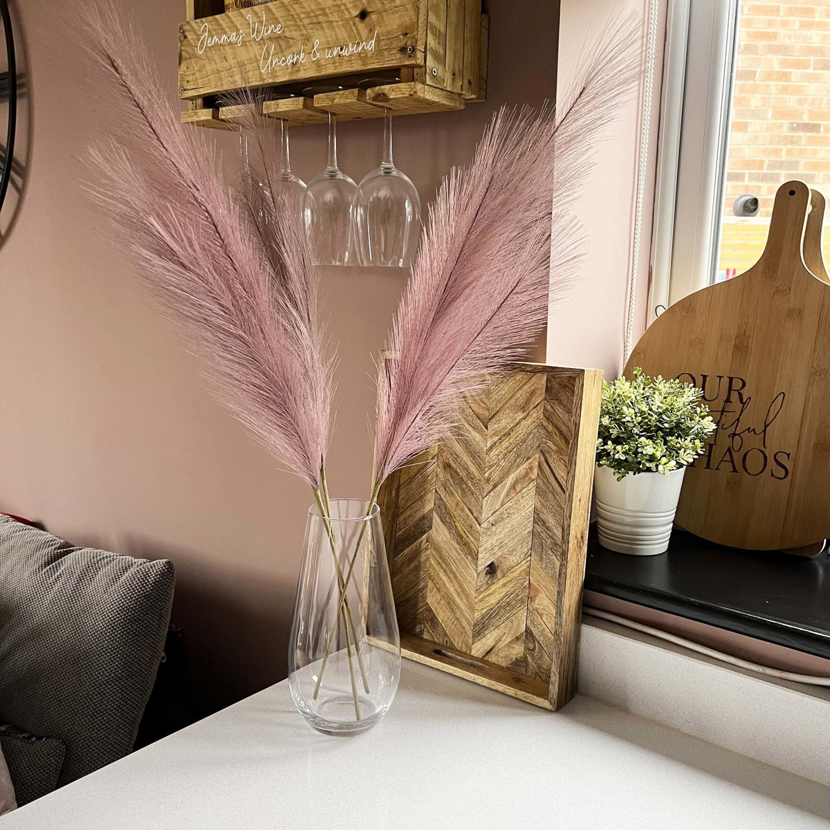 Lilac Faux Pampas Grass Stem in glass vase on kitchen bench.with plant. 