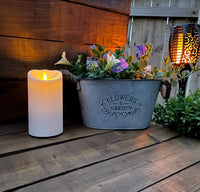 Luminara Outdoor Flameless Battery Candle lit up with Solar Light and planter full of purple flowers