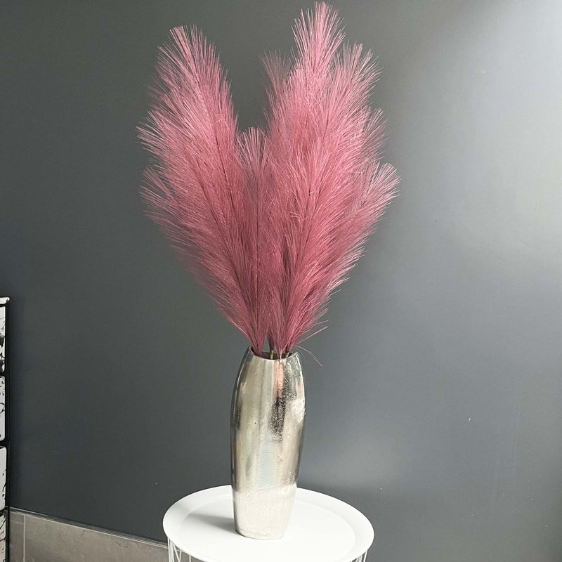 Scarlet Red Faux Pampas Grass Stem in a chrome vase with a dark grey background, on a white table.