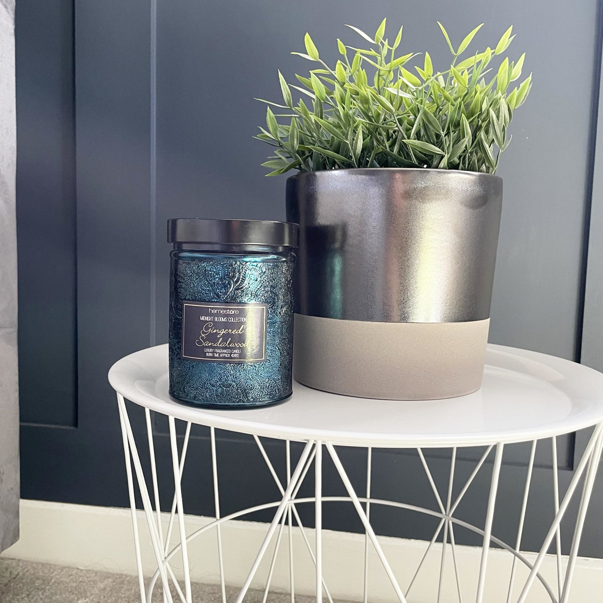 Terra Grey Metallic Style Planters with greenery in and candle, on white table against blue wall