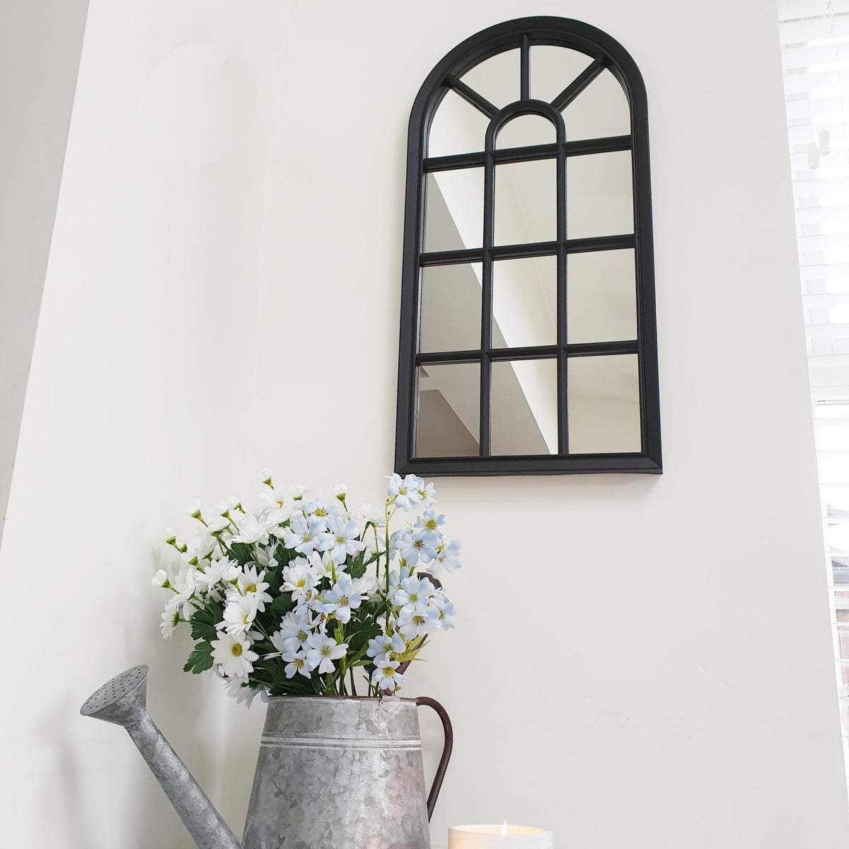 Velit Window style wall mirror in black, on a white wall with a watering can vase of flowers