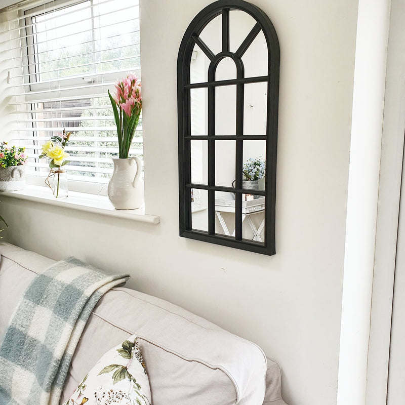 Velit Window style wall mirror in black, on a white wall with a selection of flowers on the windowsill 