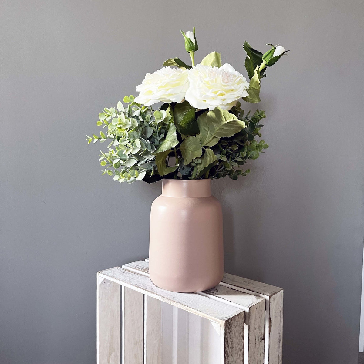 White Garden Rose Spray in a blush pink vase on a crate bench